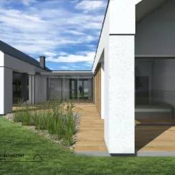 Wizualizacja projektu indywidualnego domu jednorodzinnego z drewnianym tarasem, dużymi przeszkleniami i minimalistyczną elewacją w kolorze białym, otoczonego zielenią i trawami ozdobnymi.