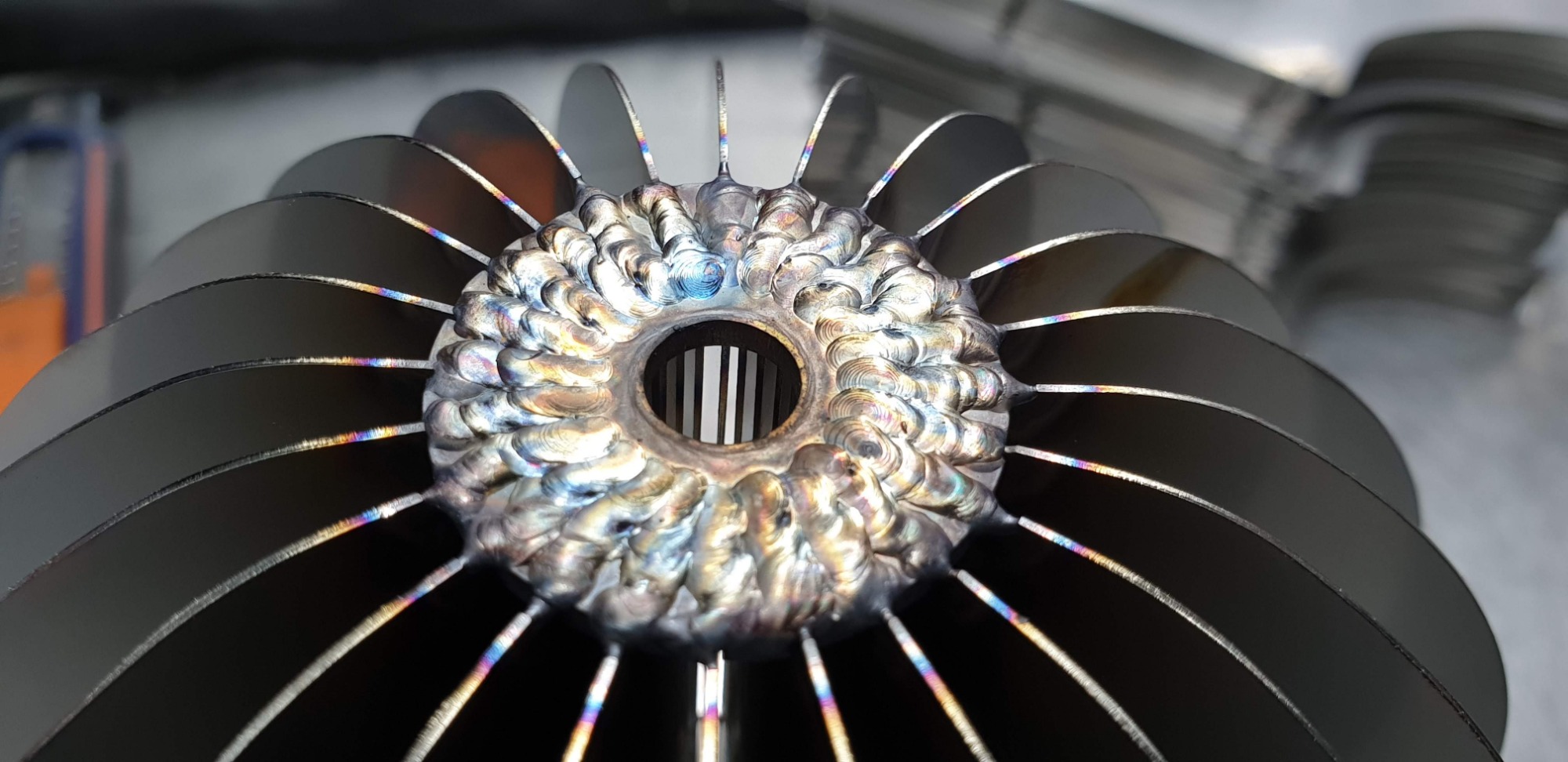 Metalowa turbina z widocznymi śladami spawania i tęczowymi przebarwieniami na krawędziach łopatek.