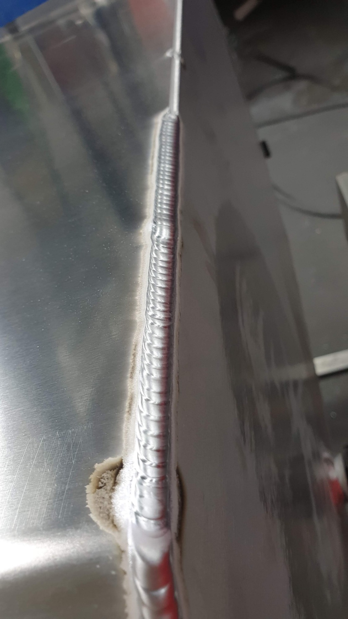 Szlifowana spoina na aluminiowej płycie, widoczny fragment zanieczyszczenia przy spoinie.