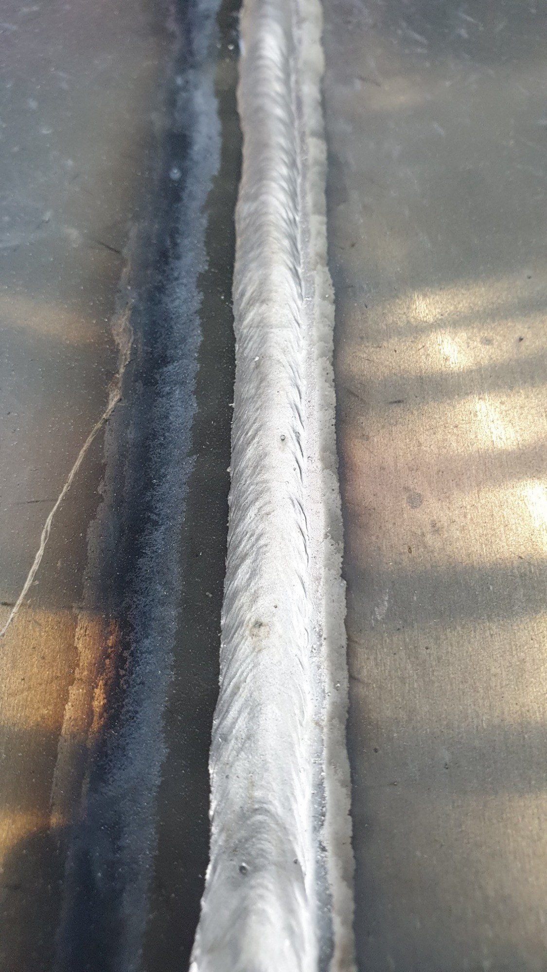 Spoina spawalnicza na metalowej powierzchni, widoczne ślady po spawaniu i zmatowienia materiału obok spoiny.