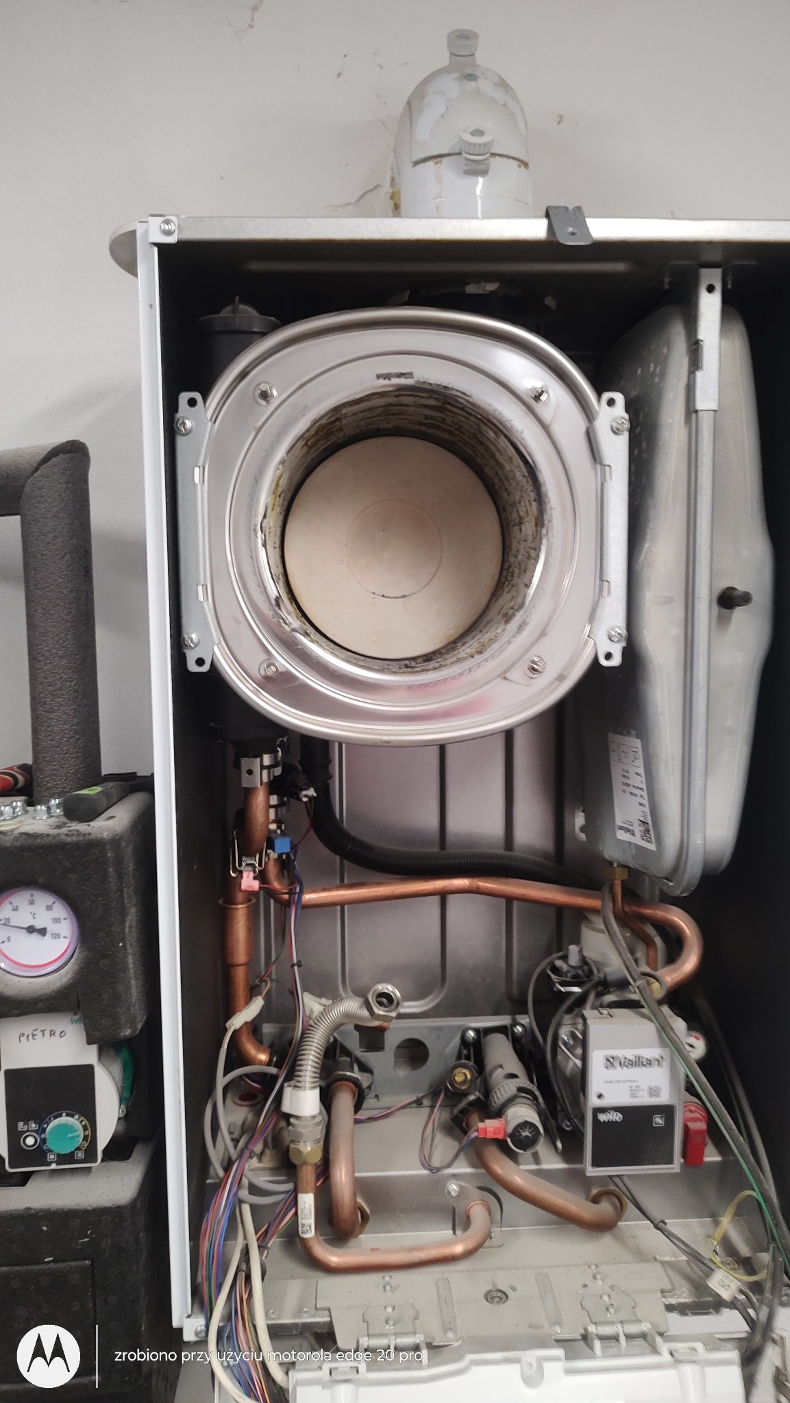 Wnętrze otwartego pieca gazowego Vaillant, widoczne miedziane rurki, przewody elektryczne oraz elementy sterujące.