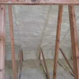 Poddasze ocieplone pianką poliuretanową, widoczne drewniane krokwie konstrukcji dachu, nierównomierna struktura piany.