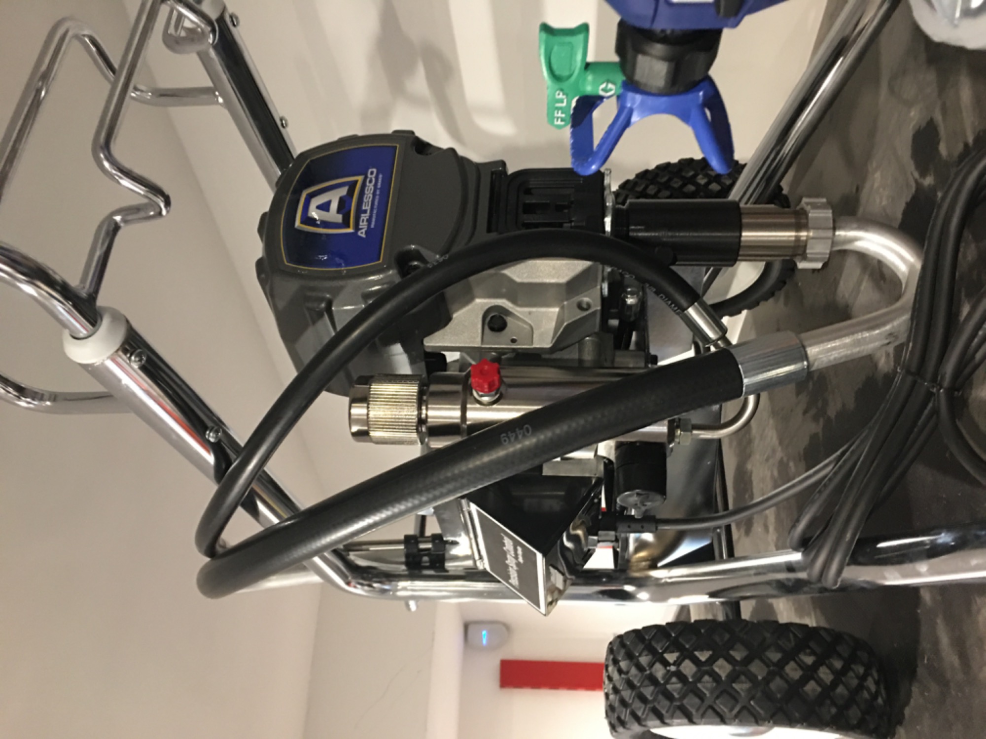 Profesjonalny agregat malarski Airlessco z chromowanymi elementami i niebiesko-żółtym logo, widoczne przewody i dysza z oznaczeniami FF LP, ustawiony na podłodze.