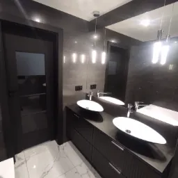 Nowoczesna łazienka w ciemnej tonacji z dwiema owalnymi umywalkami nablatowymi, podwieszaną szafką z ryflowanym frontem, lustrem i marmurową podłogą w bieli i szarości.