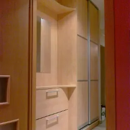 Wnęka z lustrem i dwiema szufladami w zabudowie z jasnego drewna, obok szafa przesuwna z aluminiowymi ramami, widok z korytarza.