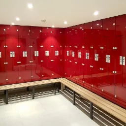 Rząd czerwonych szafek z numerami i drewnianymi ławkami w jasnym pomieszczeniu.