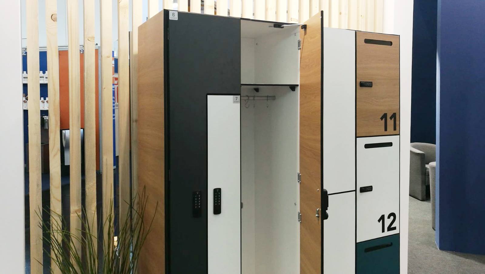 Wielokolorowe szafki ubraniowe z numerami, niektóre z otwartymi drzwiami, z zamkami elektronicznymi i drewnianymi akcentami, ustawione w pomieszczeniu z elementami dekoracyjnymi z drewna.