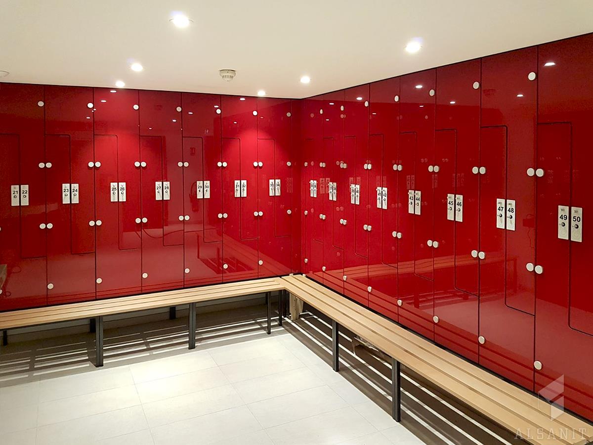 Rząd czerwonych szafek z numerami i drewnianymi ławkami w jasnym pomieszczeniu.