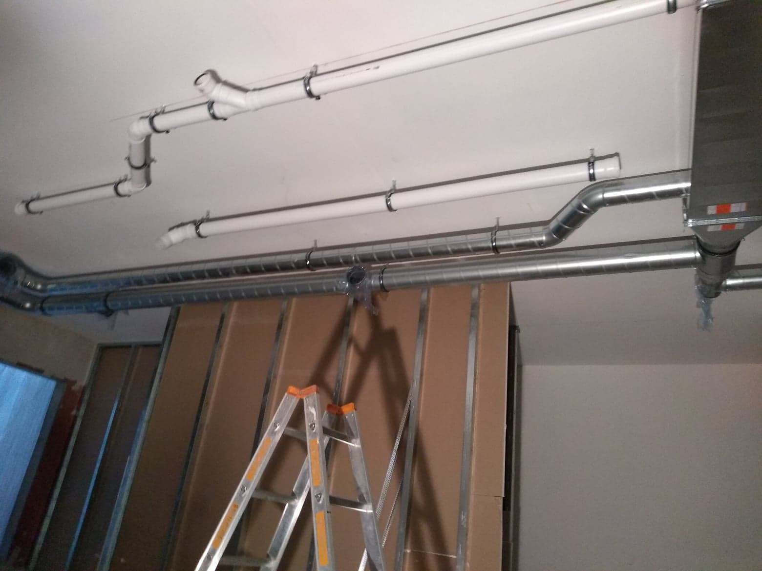 Różne rury wentylacyjne, plastikowe i metalowe, zamontowane pod sufitem w trakcie prac instalacyjnych w Skale, z widoczną drabiną i konstrukcją ścian.