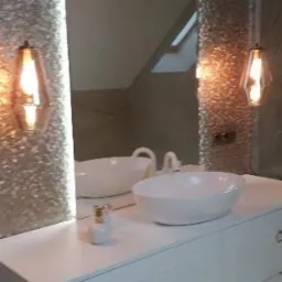 Nowoczesna łazienka z umywalką nablatową, szafką z szufladami, dekoracyjnymi lampami wiszącymi i lustrem w ozdobnej ramie.