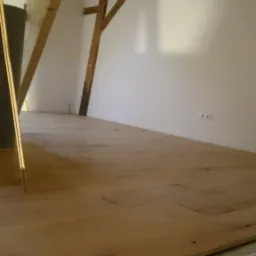 Poddasze z drewnianą konstrukcją więźby dachowej, ocieplone podłogowo z widocznym systemem ogrzewania podłogowego, przygotowane do dalszych prac wykończeniowych.