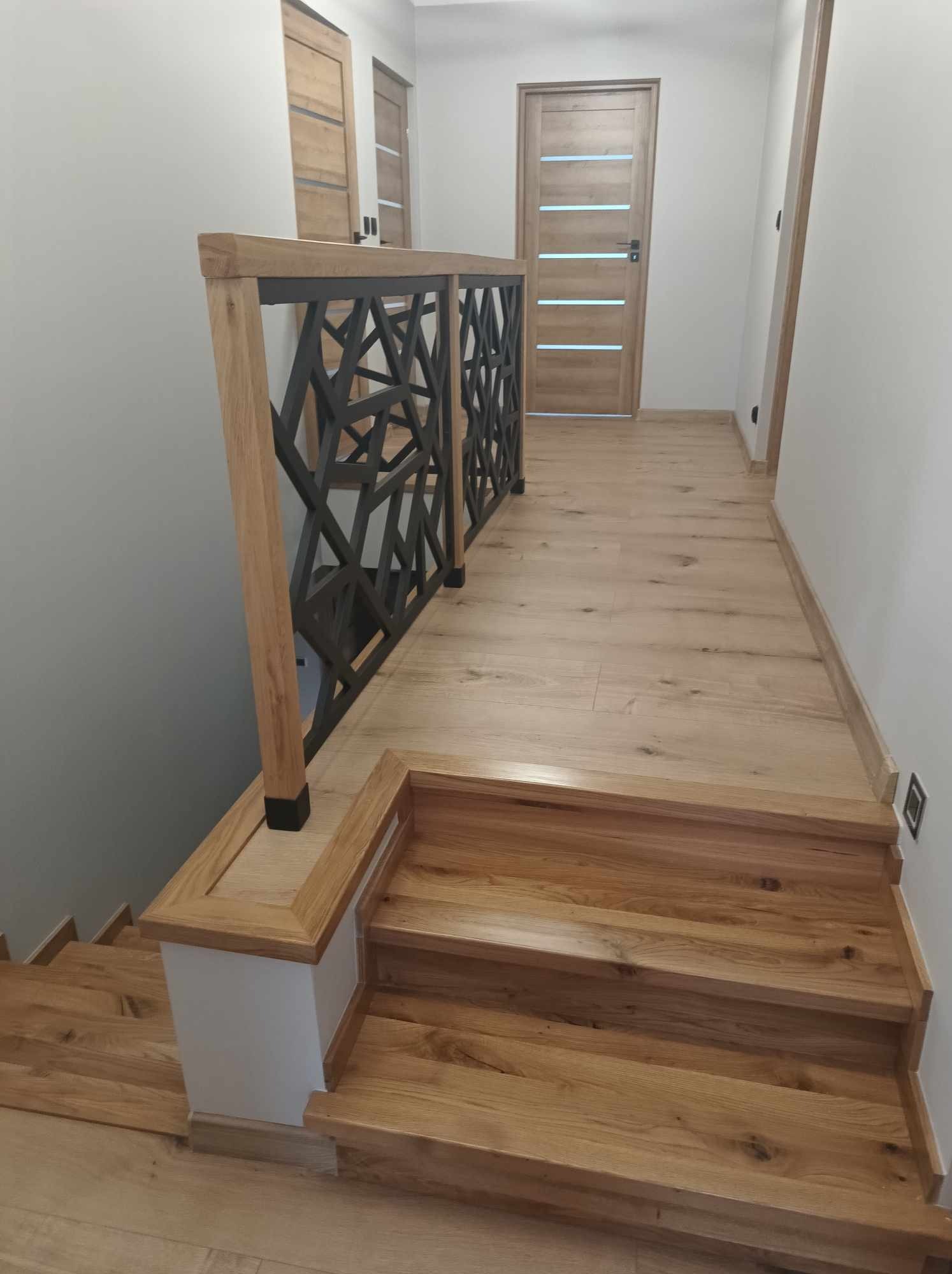 Nowoczesne schody z jasnego drewna z geometryczną, metalową balustradą i drewnianą podłogą w korytarzu.