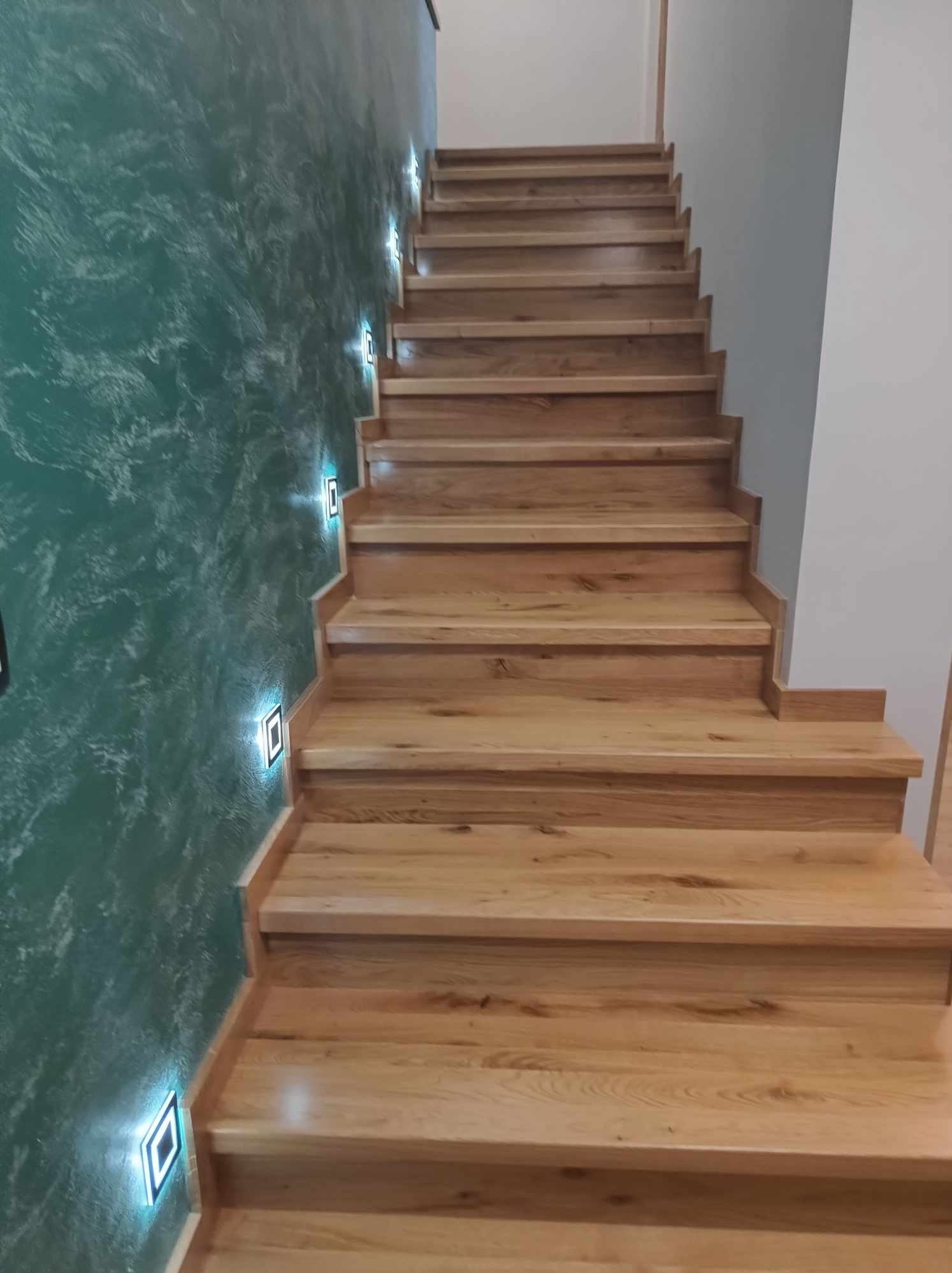 Drewniane schody z podświetleniem LED na ścianie o dekoracyjnej fakturze w Międzybrodziu Bialskim.