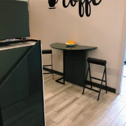 Częściowy widok nowoczesnej kuchni z blatem i dwoma składanymi stołkami barowymi, na blacie misa z pomarańczami, na ścianie dekoracja 'coffe' i motyw filiżanki, podświetlenie LED.