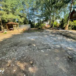 Teren po wycince drzew i krzewów, przygotowany pod budowę, widoczny zarys fundamentów, w tle altana i dom jednorodzinny.