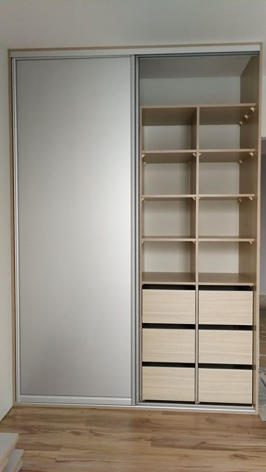 Wnętrze szafy z przesuwnymi, lustrzanymi drzwiami, z otwartą częścią regałową i szufladami, w jasnej kolorystyce drewna, na podłodze panele.