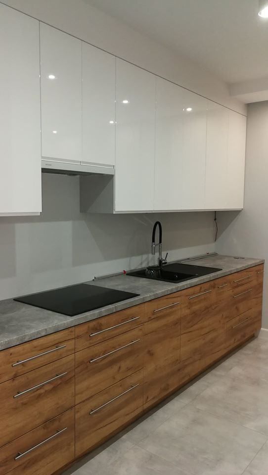 Nowoczesna kuchnia z białymi szafkami górnymi na wysoki połysk i drewnopodobnymi szafkami dolnymi z szufladami, szary blat, czarny zlew i płyta indukcyjna.