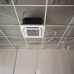 Kasetonowa jednostka klimatyzacyjna zamontowana w suficie podwieszanym w trakcie prac wykończeniowych, widoczne przewody instalacyjne i konstrukcja sufitu.