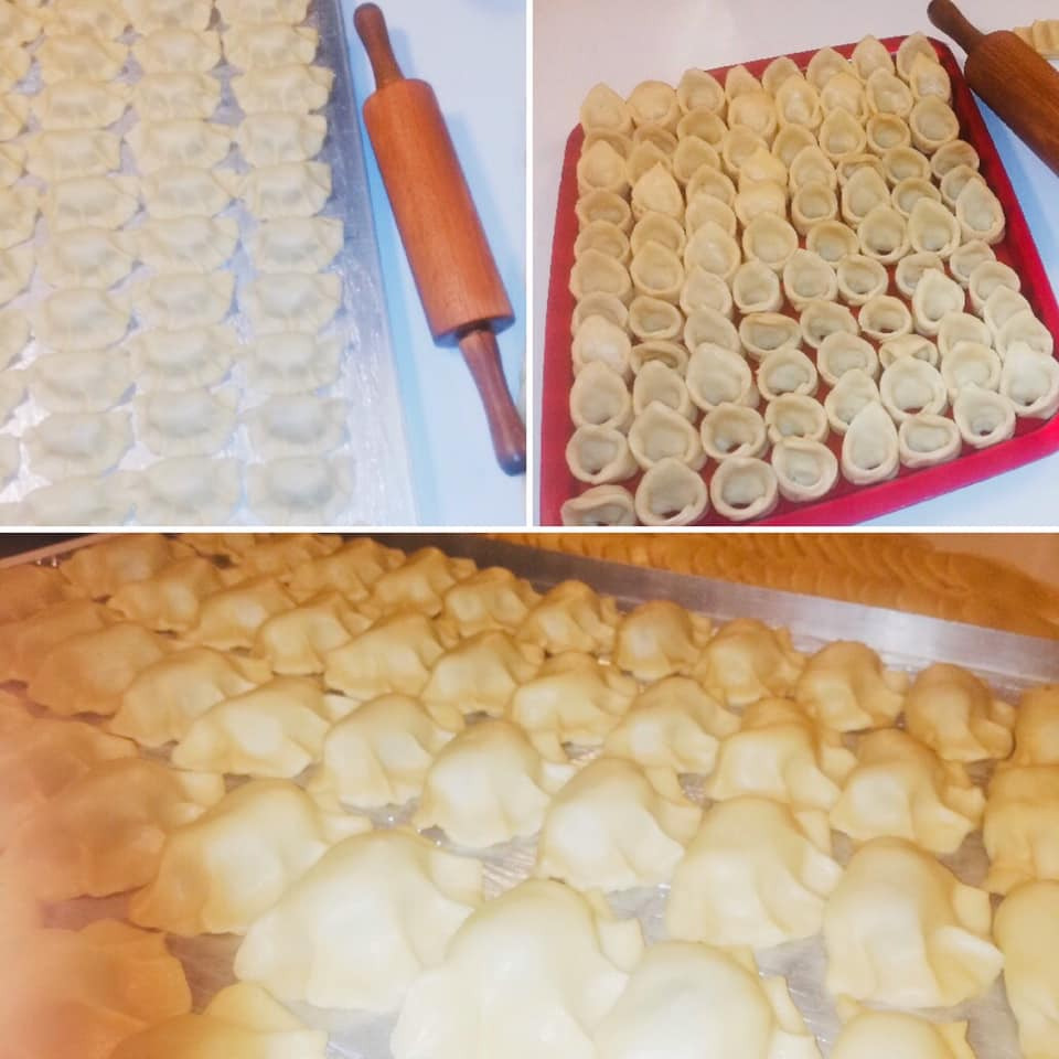 Ręcznie robione pierogi ułożone na blaszkach i czerwonej tacy, obok drewniany wałek do ciasta.