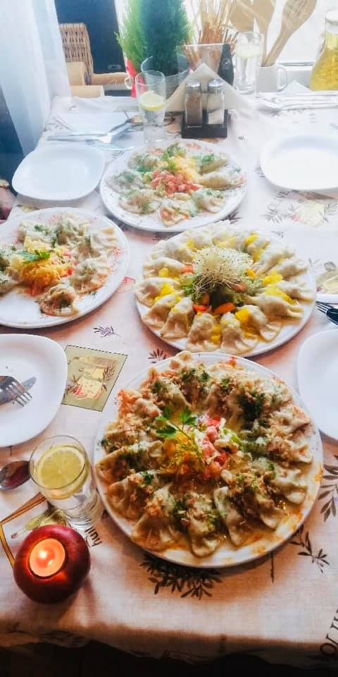 Uroczysty stół nakryty do posiłku z czterema talerzami pierogów z różnymi dodatkami, szklanką z cytryną i świeczką w kształcie jabłka.