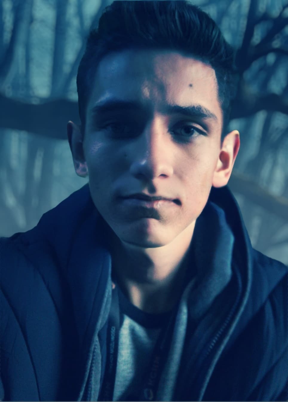 Portret młodego mężczyzny z Przemkowa w kurtce na tle drzew, prawdopodobnie pracownika firmy remontowej, z widoczną smyczą identyfikacyjną.