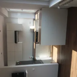 Nowoczesna, jasna kuchnia z białymi frontami szafek i drewnianymi akcentami, widziana z góry w mieszkaniu w Zaborzu. Widoczne okno dachowe i fragment drewnianej podłogi.