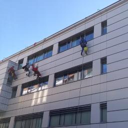AlpinZerg Sp.z o.o - Pracownicy alpinistyczni na linach podczas mycia okien w budynku biurowym z nowoczesną elewacją w słoneczny dzień.