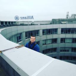 AlpinZerg Sp.z o.o - Pracownik w uprzęży na dachu budynku biurowego z widocznym logo firmy Allianz w tle.