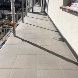 Group - Wykończony balkon w nowym budownictwie z szarymi płytkami podłogowymi i widocznym rusztowaniem z zabezpieczeniami.