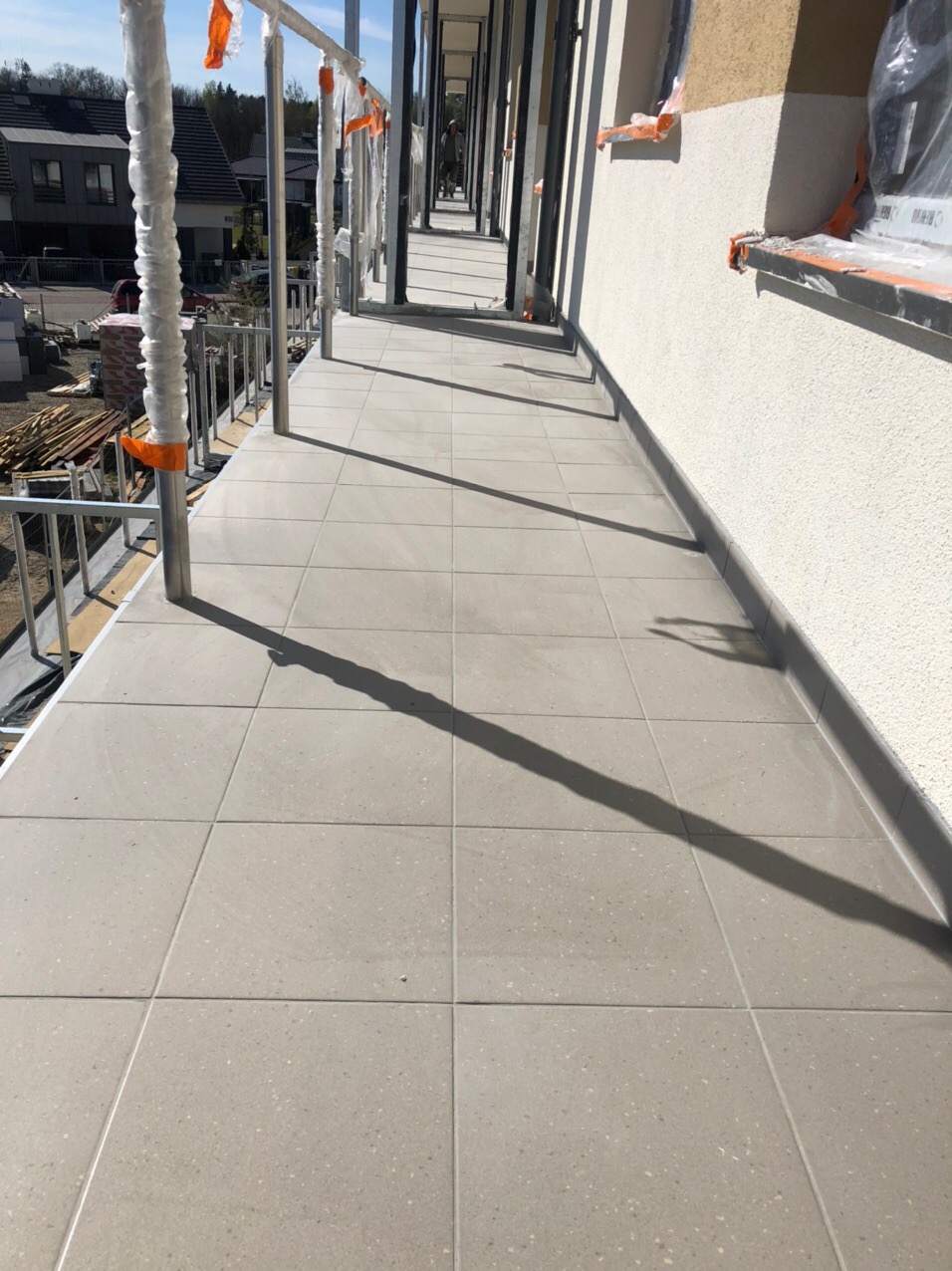 Wykończony balkon w nowym budownictwie z szarymi płytkami podłogowymi i widocznym rusztowaniem z zabezpieczeniami.