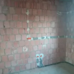 Surowa ściana z cegły z rozprowadzoną instalacją elektryczną w peszlach i puszkach, widoczne przygotowane punkty pod gniazdka i włączniki.