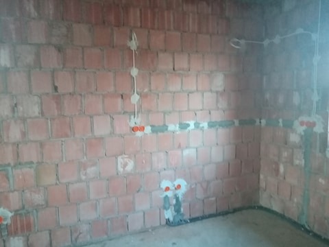 Surowa ściana z cegły z zamontowanymi puszkami elektrycznymi i przewodami w szarym peszlu, widoczne przygotowania do rozprowadzenia instalacji elektrycznej.