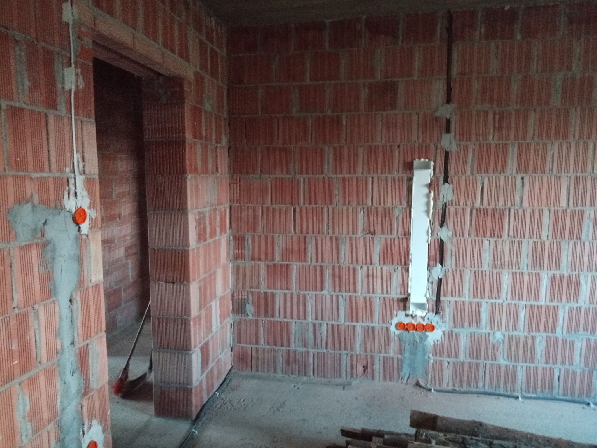 Surowy mur z cegły z widocznymi przewodami elektrycznymi w bruzdach, puszki instalacyjne osadzone w zaprawie, widok na wnętrze w trakcie prac.