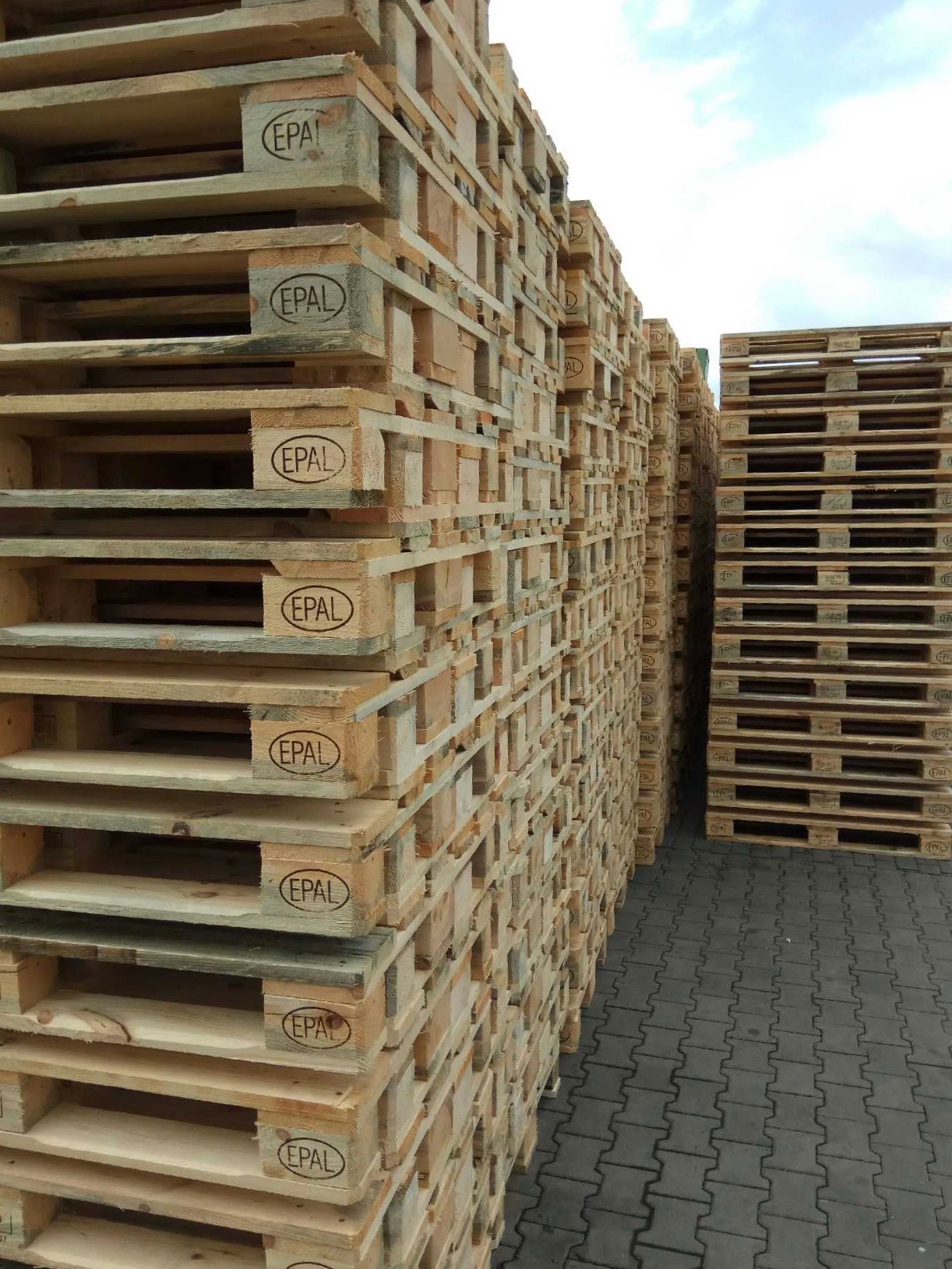 Stosy drewnianych palet EPAL ułożone na kostce brukowej, widoczne znaki certyfikacji EPAL na paletach.