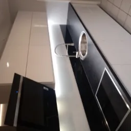 Nowoczesna kuchnia z białymi szafkami, czarnym blatem, stalowym zlewozmywakiem i płytą indukcyjną oraz pochłaniaczem pary, widok z dołu.