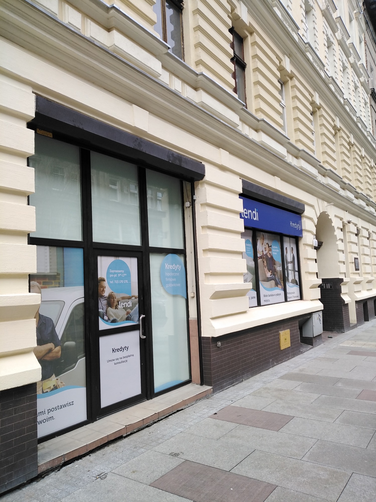 Fasada budynku z biurem kredytowym 'lendi', z widocznymi plakatami reklamowymi w oknach, informującymi o możliwości umówienia się na bezpłatną konsultację kredytową.