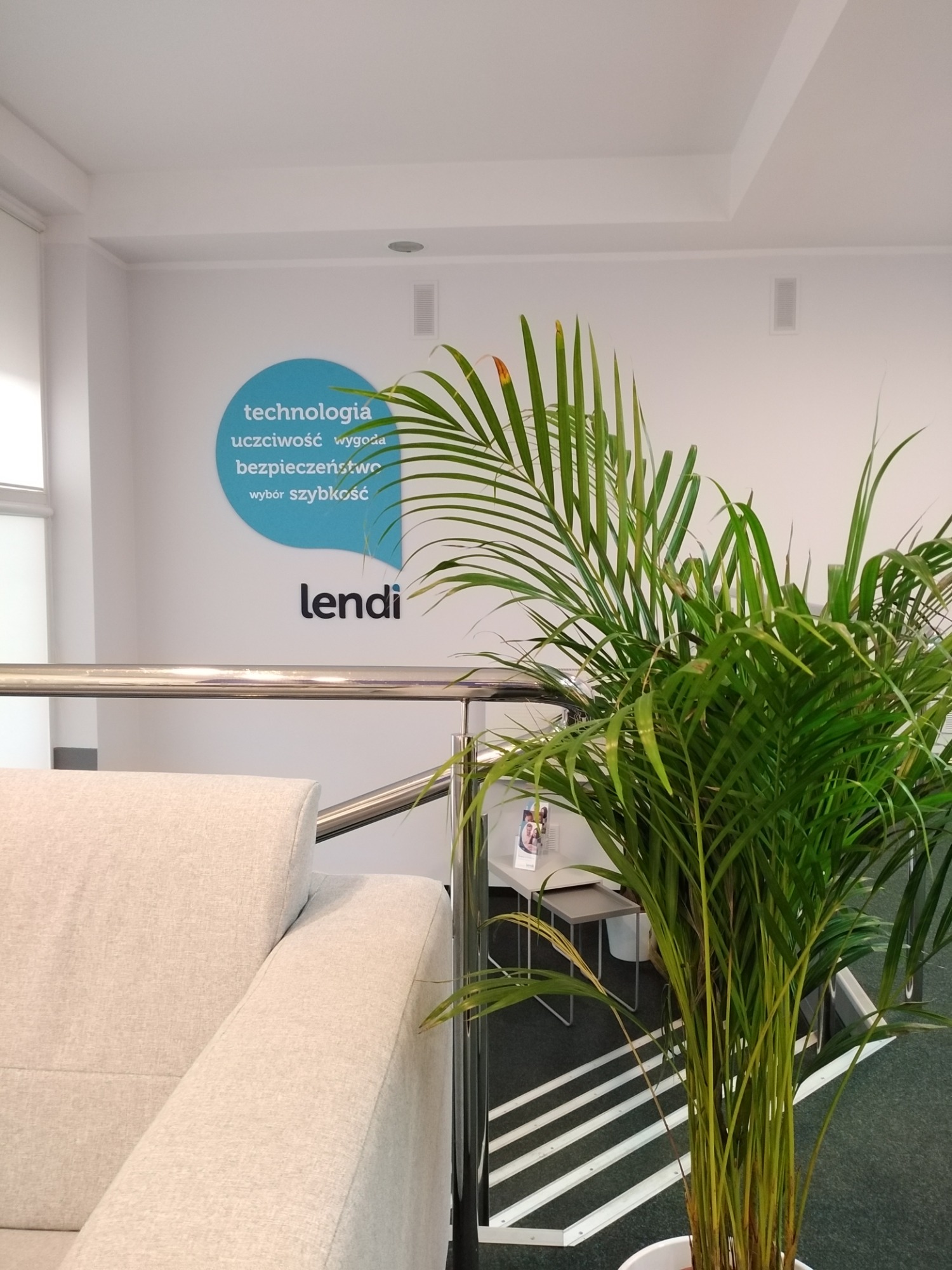 Wnętrze biura w Szczecinie z logo firmy 'lendi' na ścianie, sofa i roślina doniczkowa w recepcji.