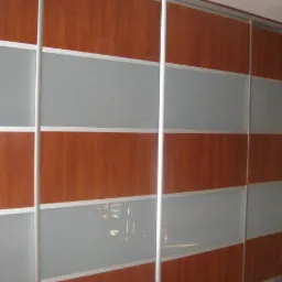 Przesuwne drzwi szafy wnękowej z panelami z drewna wiśniowego i matowego szkła, aluminiowe obramowanie.