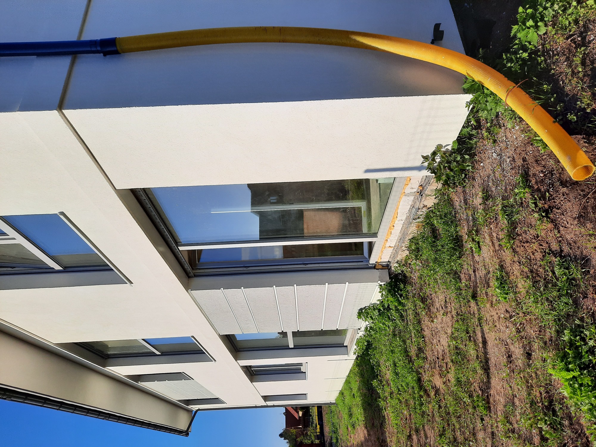 Nowoczesna elewacja budynku z oknami, widoczna żółta rura wentylacyjna na tle świeżo obsianej trawy.