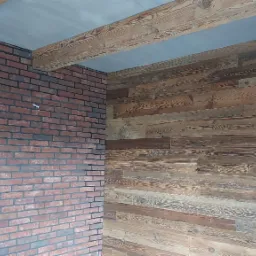 Wnętrze z ceglaną ścianą i drewnianą boazerią z widocznymi belkami stropowymi, prezentujące połączenie rustykalnego i nowoczesnego stylu.