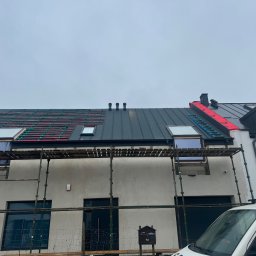 S-bud Sylwester Bonk - Dom w trakcie krycia dachu blachą na rąbek stojący, widoczne rusztowania i okna dachowe. Część dachu pokryta, część w trakcie prac.