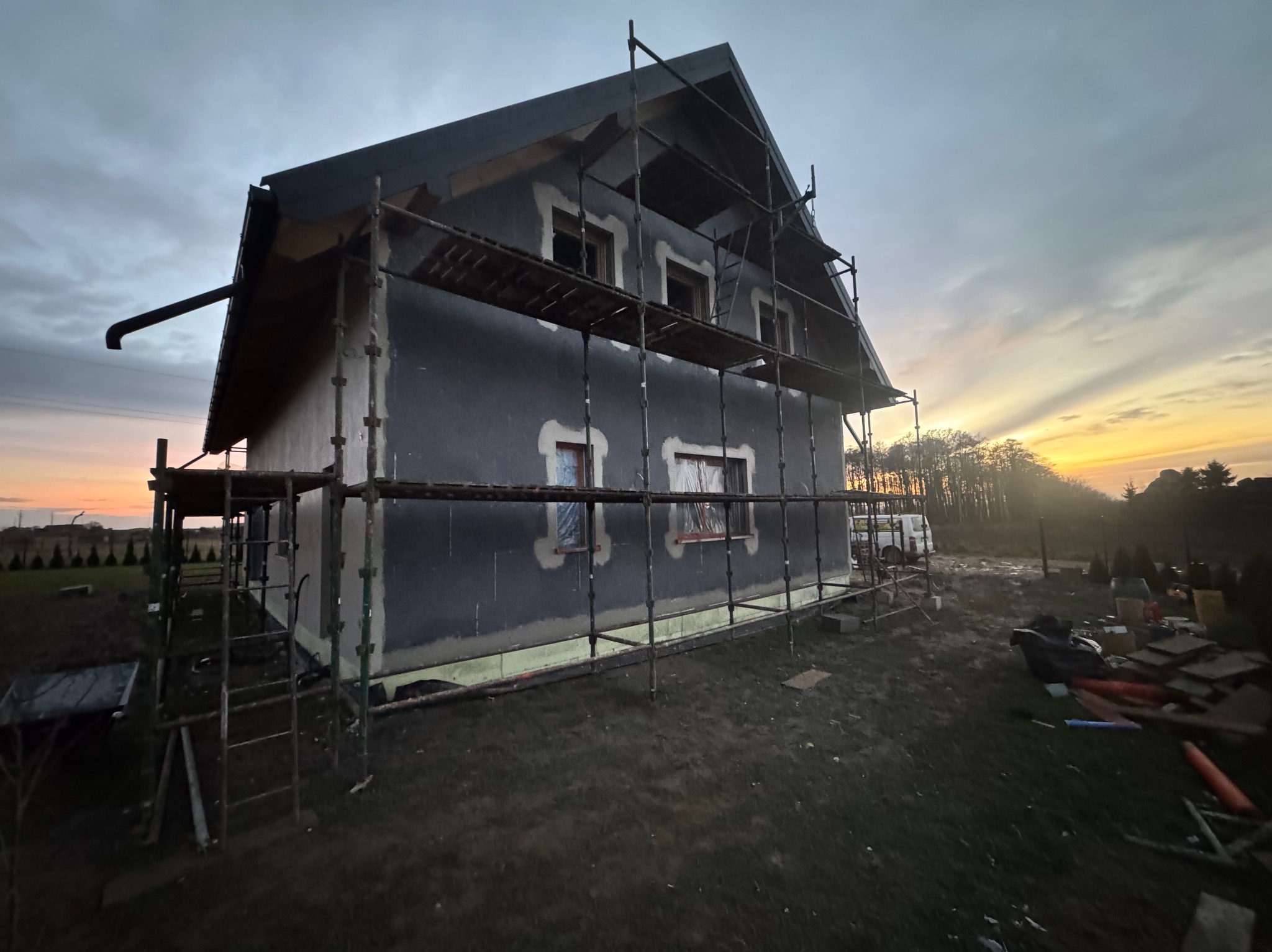 Dom w trakcie ocieplania w Gniewinie, widoczne rusztowania i przygotowana elewacja. W tle zachodzące słońce.