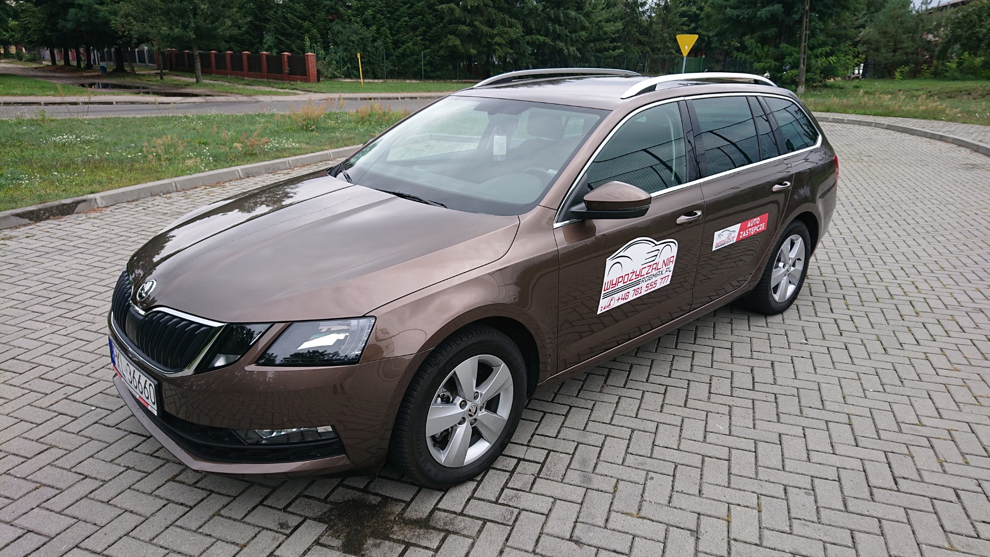 Brązowa Skoda Octavia kombi z naklejkami wypożyczalni samochodów na karoserii, zaparkowana na kostce brukowej.