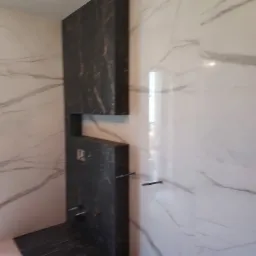 Nowoczesna łazienka z marmurowymi płytkami w odcieniach bieli i czerni, z zabudową stelaża WC w formie czarnej kolumny.