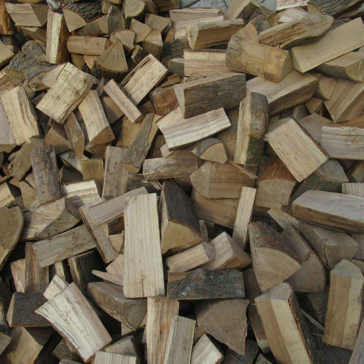 Stos pociętego drewna opałowego, różnej wielkości szczapy z widoczną korą, przygotowane do sezonu grzewczego.