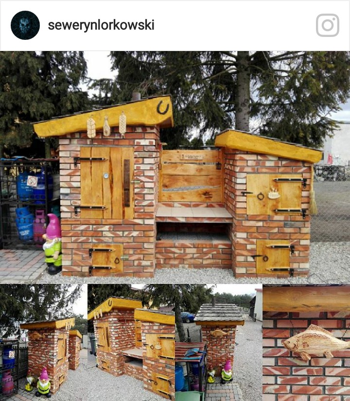 Murowana konstrukcja z cegły z drewnianymi elementami, przypominająca piec chlebowy i wędzarnię z żółtym dachem, ozdobiona drewnianymi zawieszkami i podkową, obok butle gazowe i figurka krasnala...