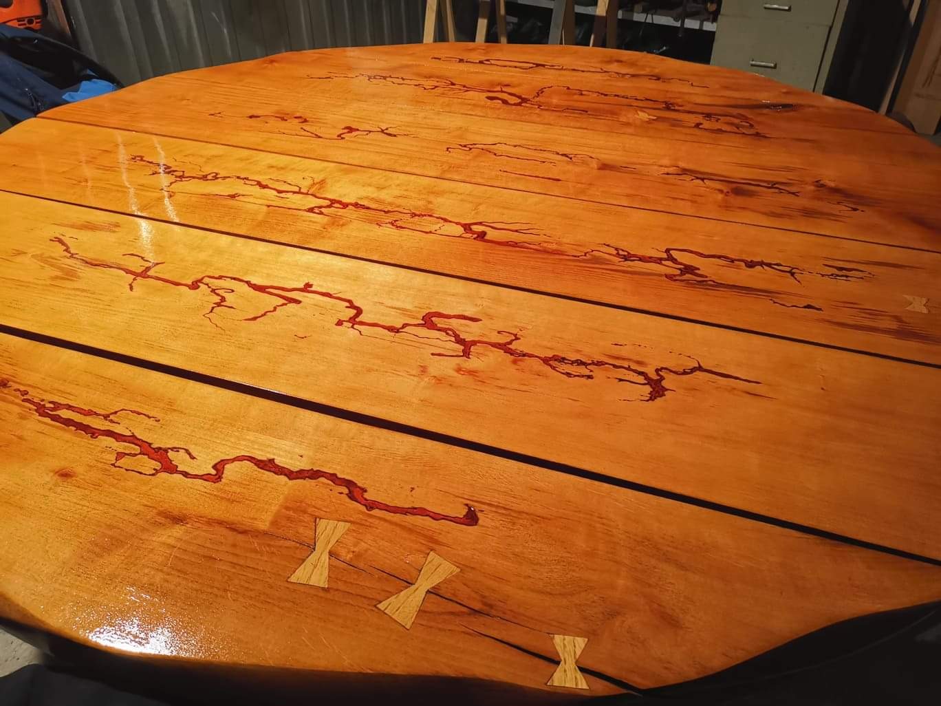 Okrągły stół z drewna z żywicą epoksydową w kolorze czerwonym, widoczne wstawki w kształcie motylków.