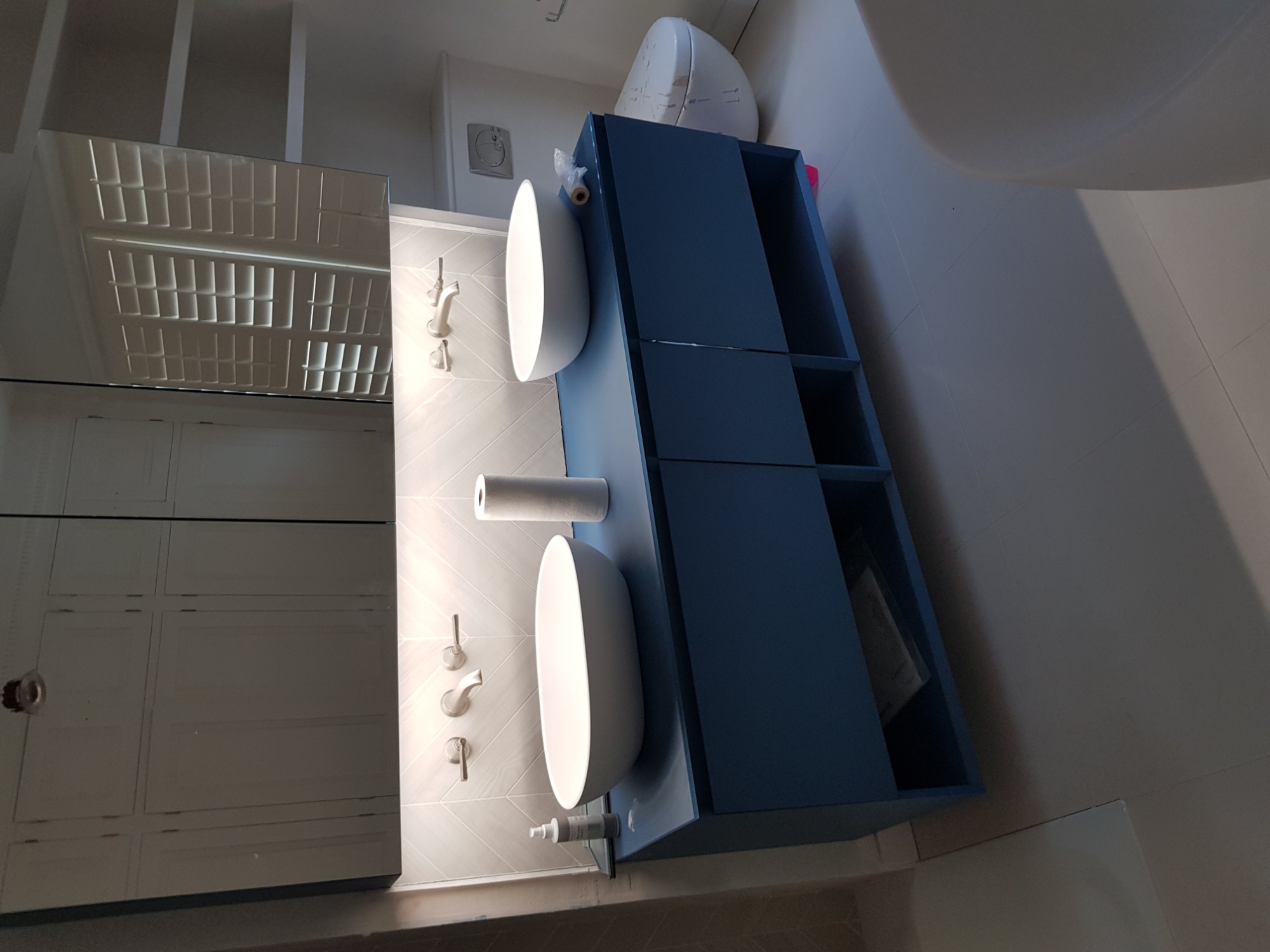 Nowoczesna łazienka z podwójną umywalką nablatową, szafką w kolorze granatowym, białą armaturą i chevronową płytką na ścianie.