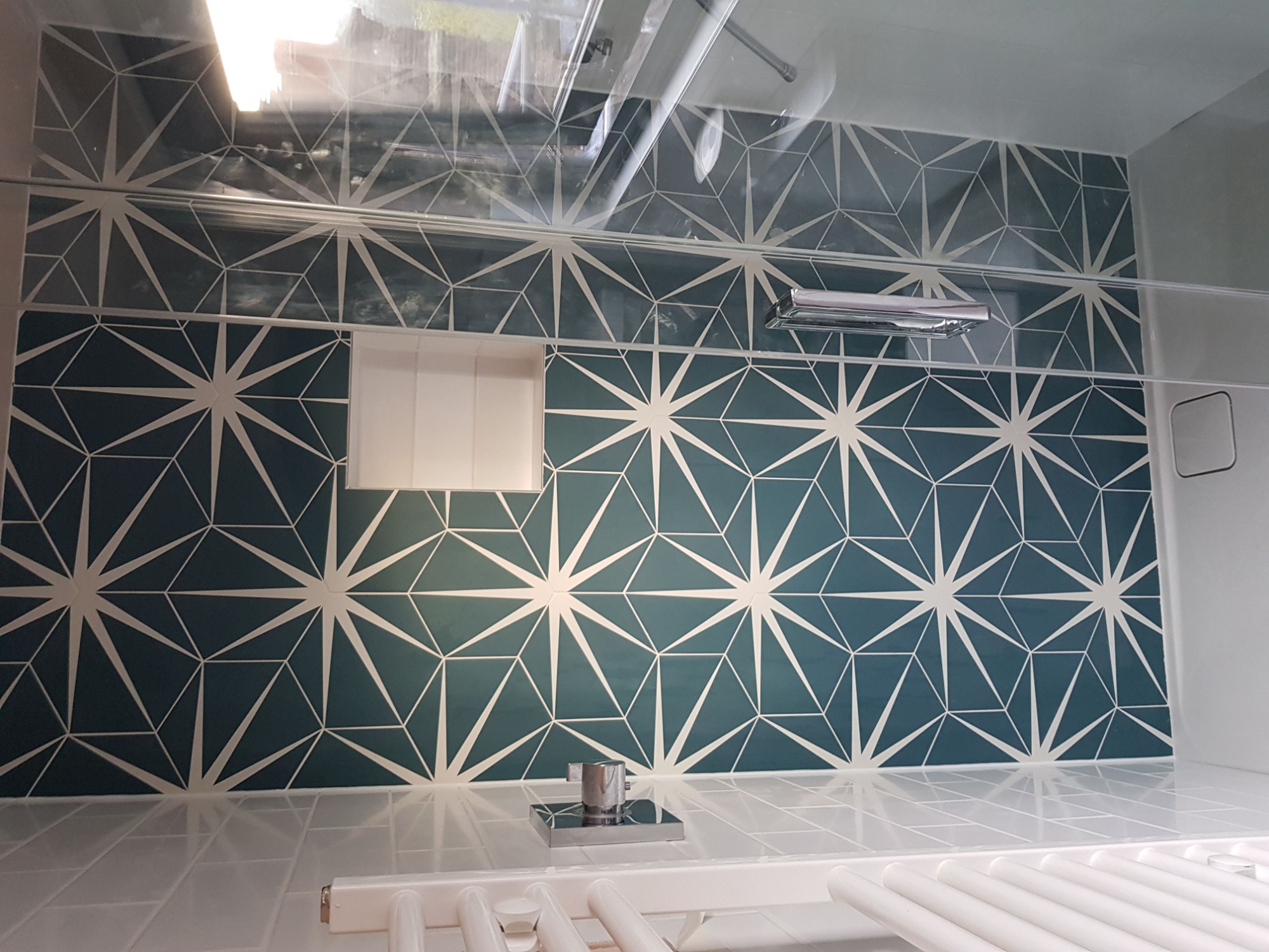 Niebiesko-białe płytki ścienne z geometrycznym wzorem gwiazd w łazience, widoczny fragment baterii umywalkowej i grzejnika drabinkowego.