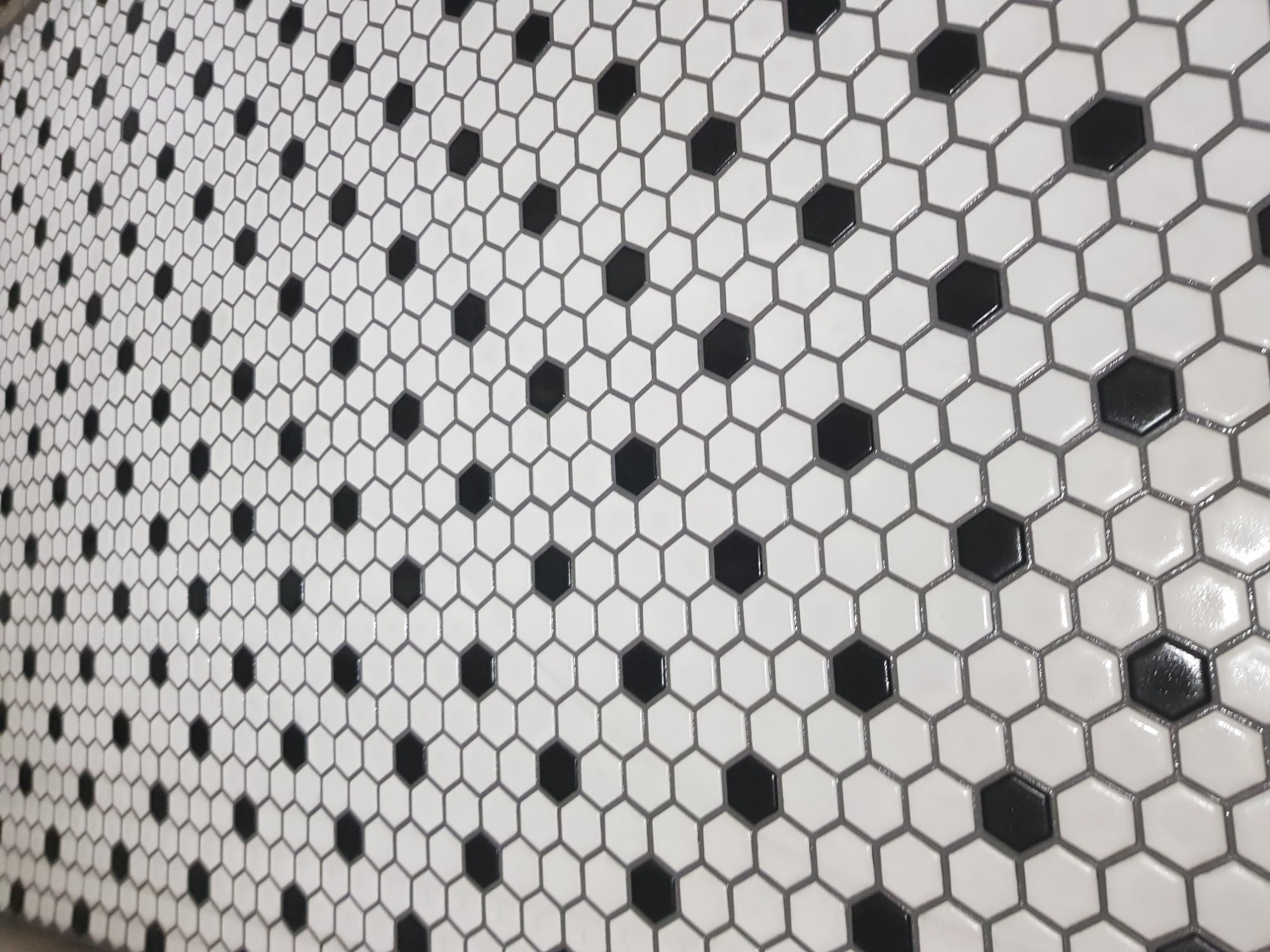 Białe, heksagonalne płytki z czarnymi akcentami ułożone na ścianie, widoczne pod kątem, z delikatnym połyskiem.